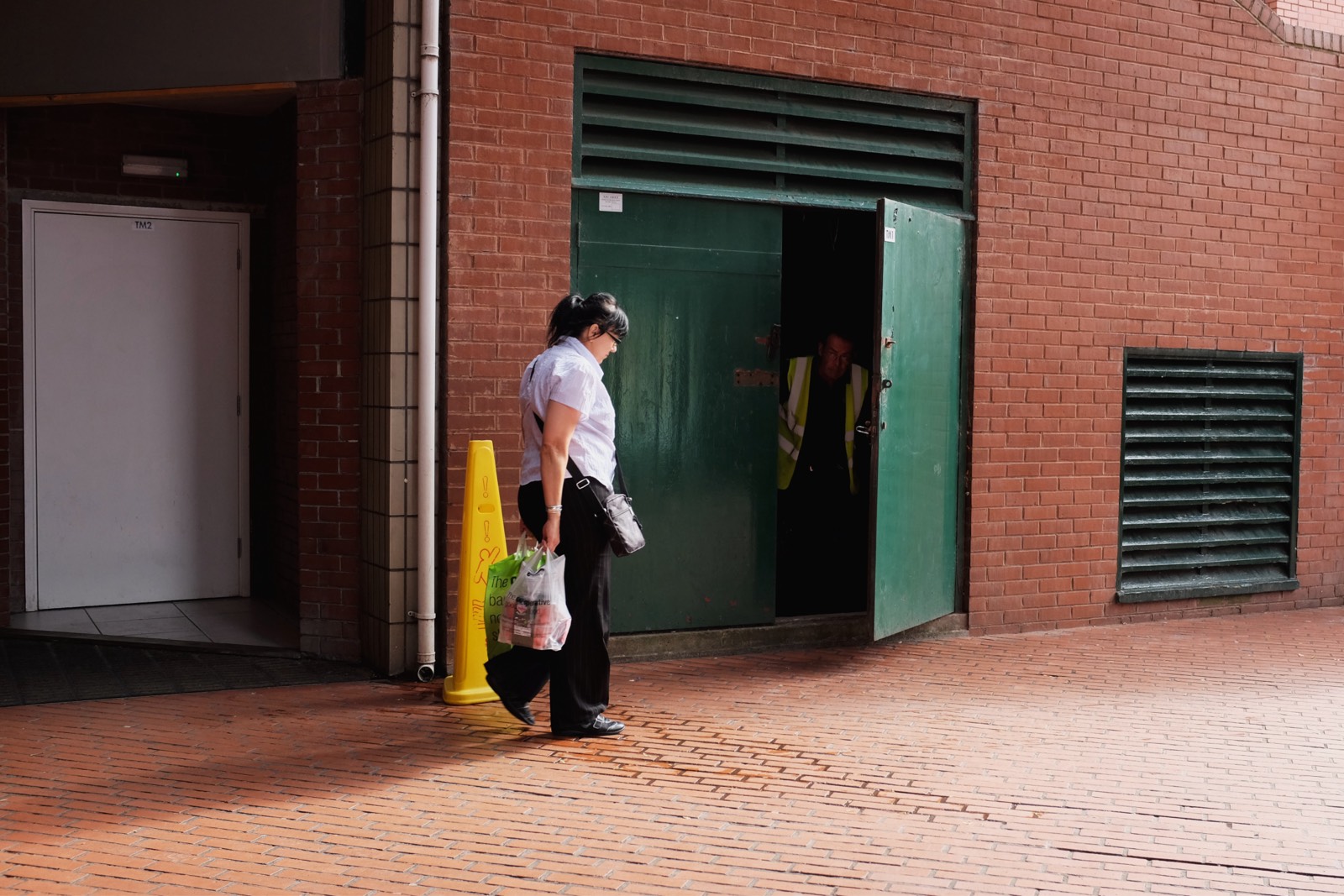 A man wearing high visibility emerges out of the dark through a door on a street just in front of a pedestrian