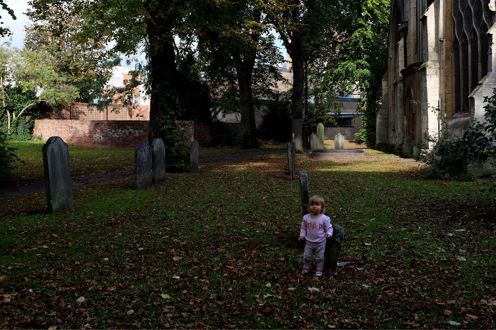 Photo of a young toddler standing in a graveyard next to a gravestone