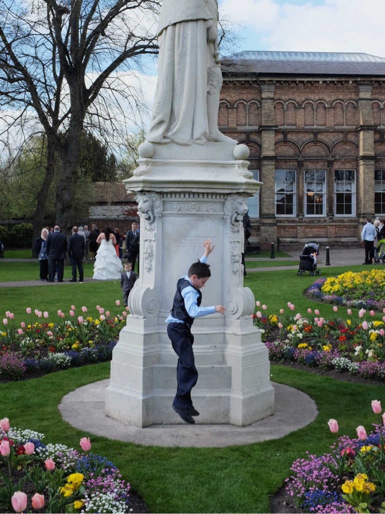 Photo of a smartly dressed boy jumping off the base of a statue in a park