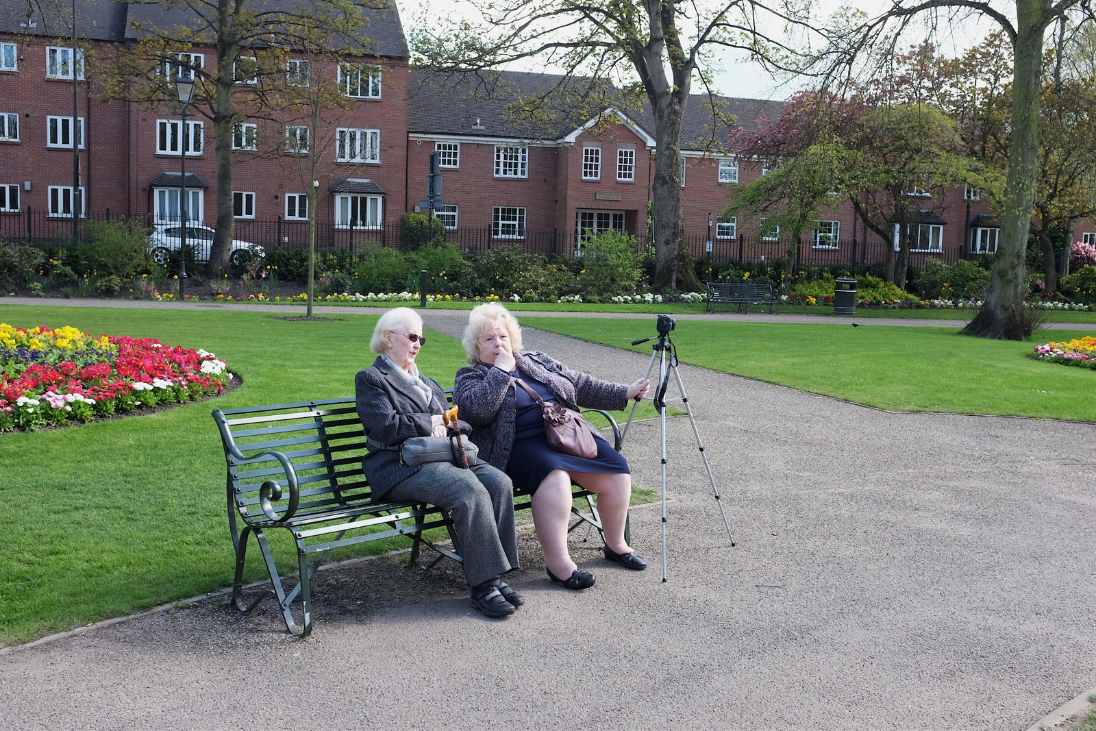 Photo of two ladies sitting on a park bench, one of them holding a camera tripod